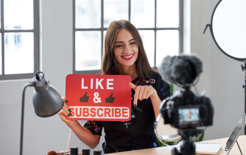 Smiling content creator recording a video, holding a 'Like & Subscribe' sign, promoting lucrative opportunities on YouTube.